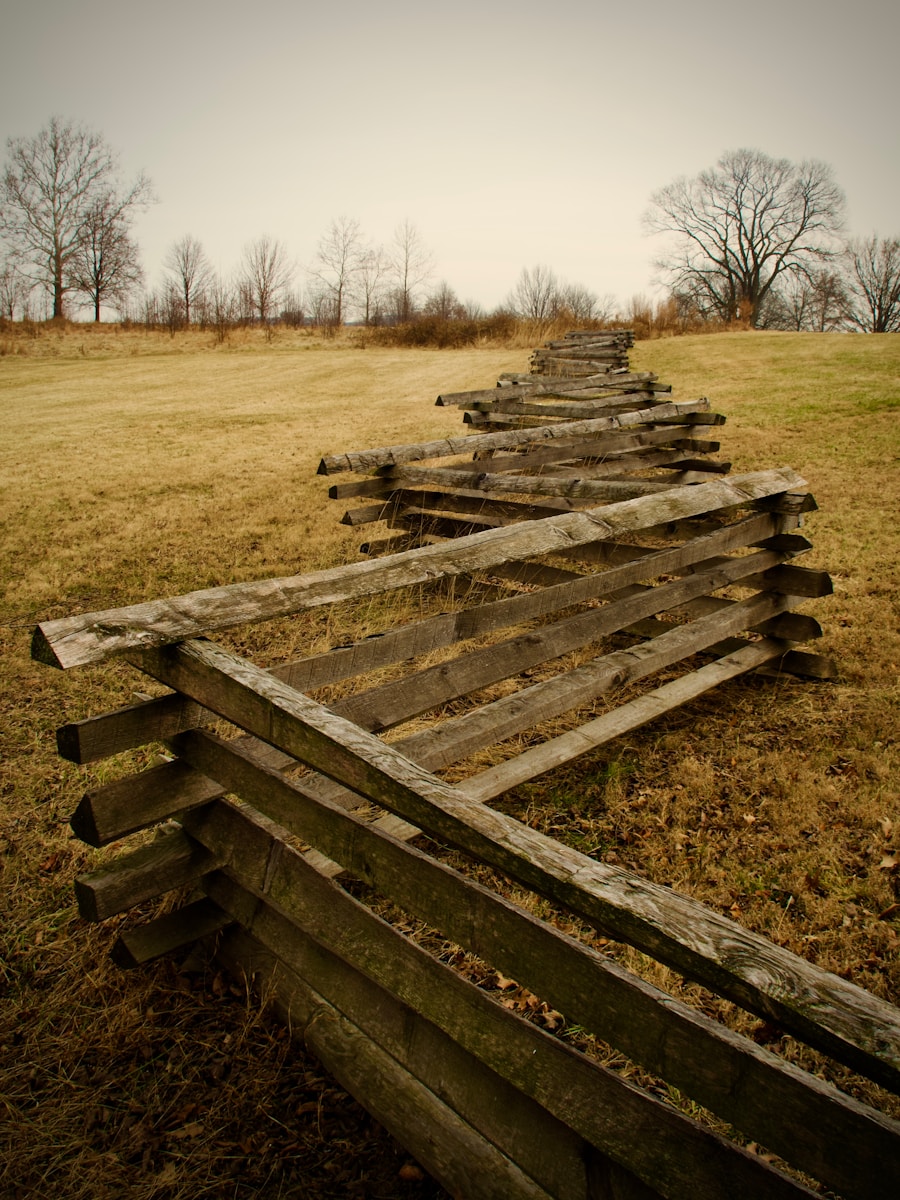 Weathered wooden fence winding through a dry grassy field.